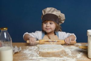 adorable-baby-girl-pursing-lips-having-mysterious-look-while-rolling-dough-by-herself